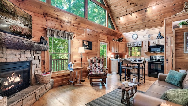 A cozy cabin interior with a stone fireplace, wooden floors, a dining area, and a kitchen with modern appliances. - Family friendly cabin in great location! Arcade~Hot Tub~Foosball~Fireplace (Sevierville)