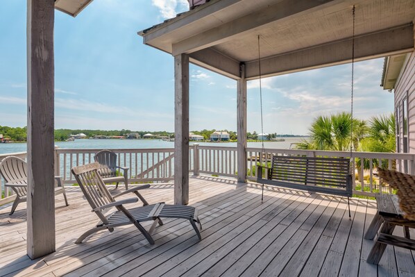 A wooden deck with a swing chair, a table, and a bench.