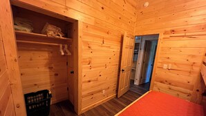 A wooden cabin room with a bed, a closet, and a door leading to another room. - Miners Cabin - Pictured Rocks Lodging (Munising)