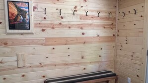 A sauna room with wooden walls, a bench, and hooks for towels. - Miners Cabin - Pictured Rocks Lodging (Munising)