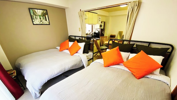 A hotel room with two beds, each with white bedding and orange pillows, a small desk with a chair, and a mirror on the wall. - 1minute walk to stataion, direct bus to Haneda Airport! Easy access! (大田区)