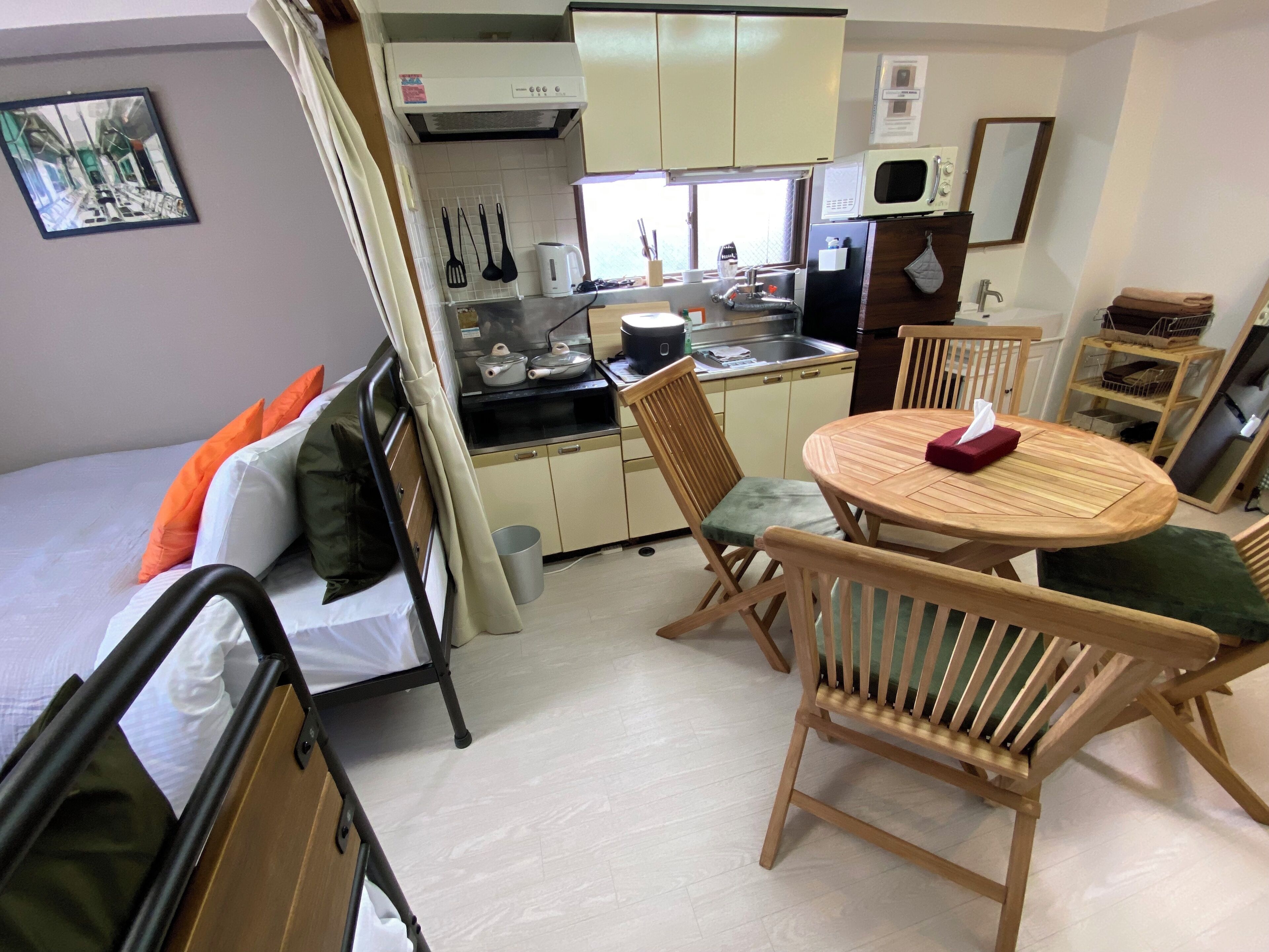 A compact bedroom with a bed, a small kitchenette, and a dining area with a table and chairs.