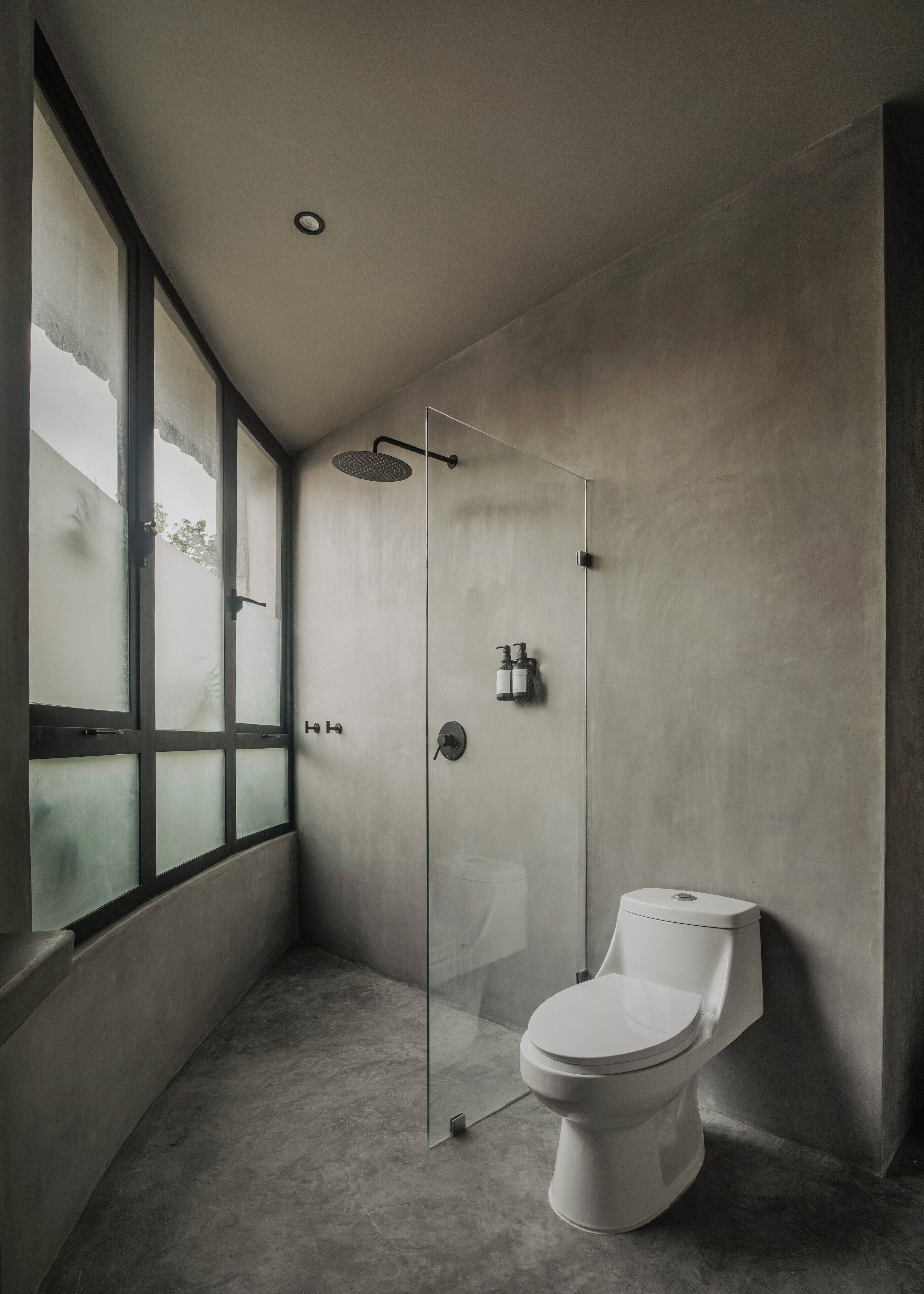 A modern bathroom with a glass-enclosed shower, a toilet, and a large window providing natural light.