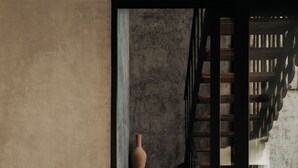 Eine Treppe mit Holzgeländer und einer Betonwand. Eine große Vase steht links auf dem Boden.
