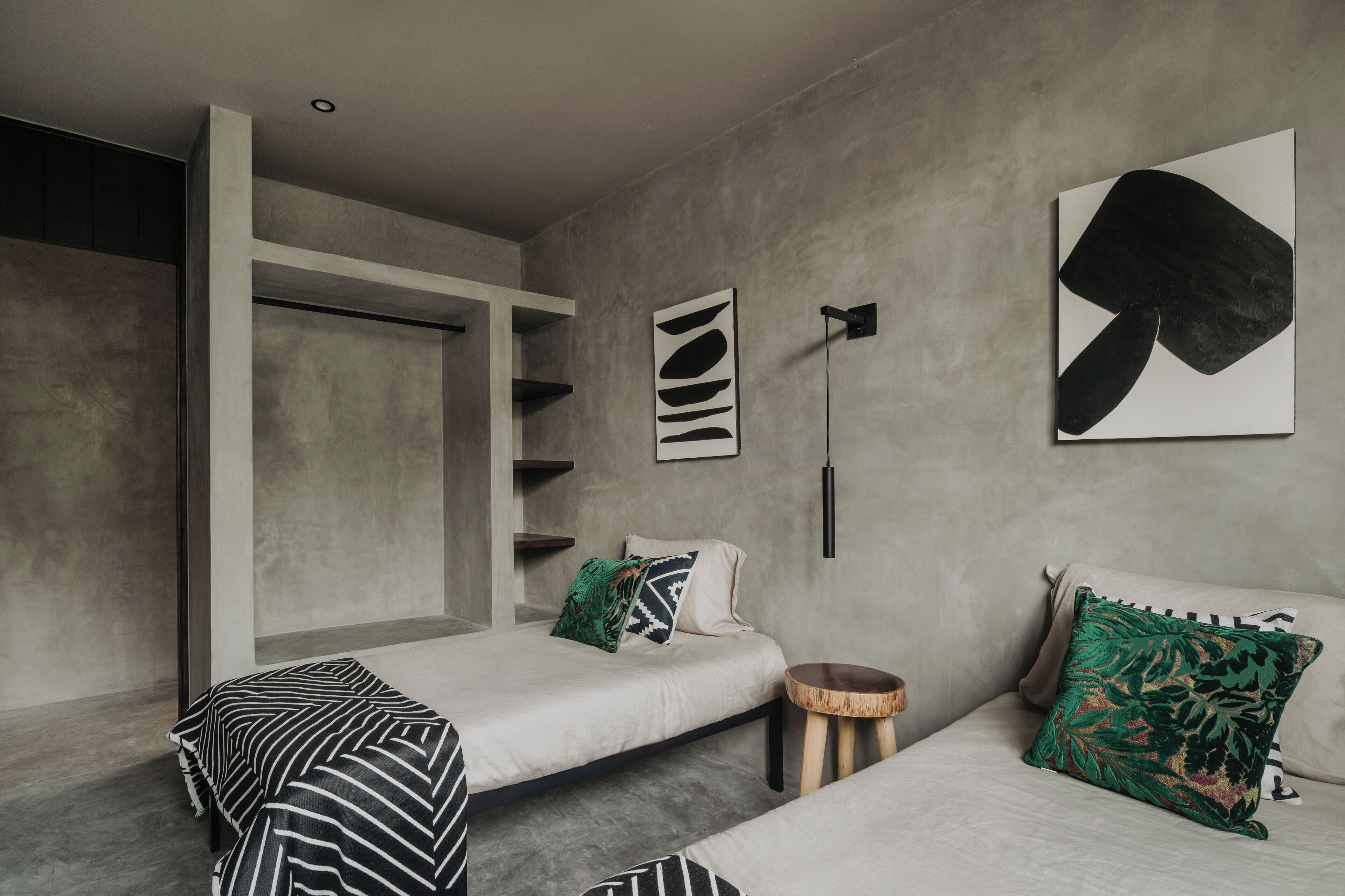 Ein modernes Schlafzimmer mit zwei Betten, einer Betonwand und abstrakter Kunst.