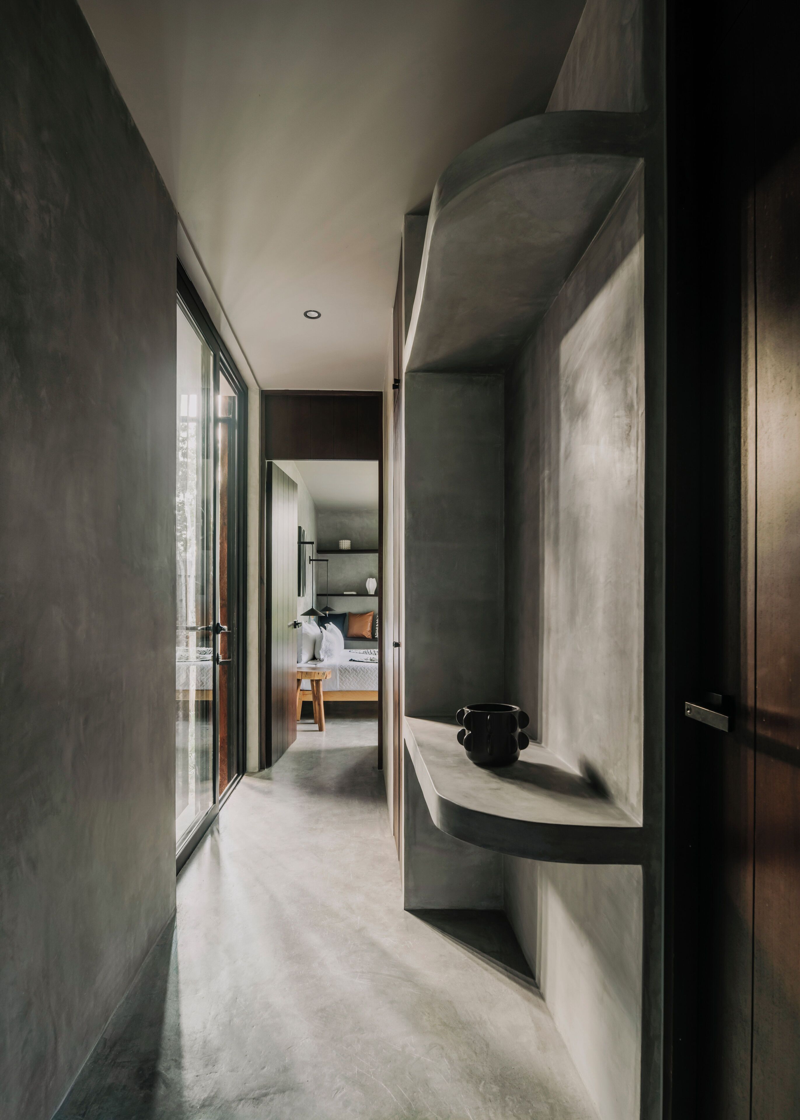A modern interior with a curved shelving unit, a wooden bench, and a bed in the background.