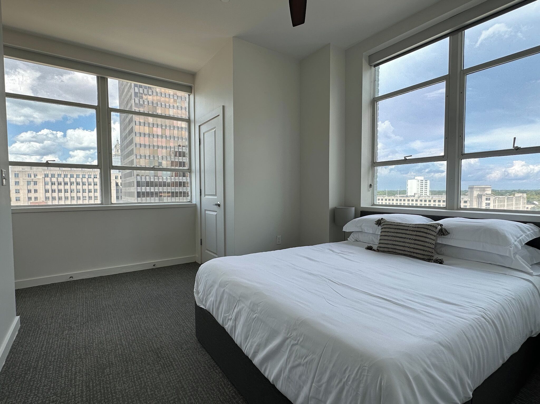A hotel room with a large bed, two windows, a door, and a carpeted floor.
