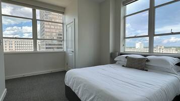 A hotel room with a large bed, two windows, a door, and a carpeted floor.