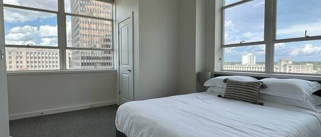 A hotel room with a large bed, two windows, a door, and a carpeted floor.