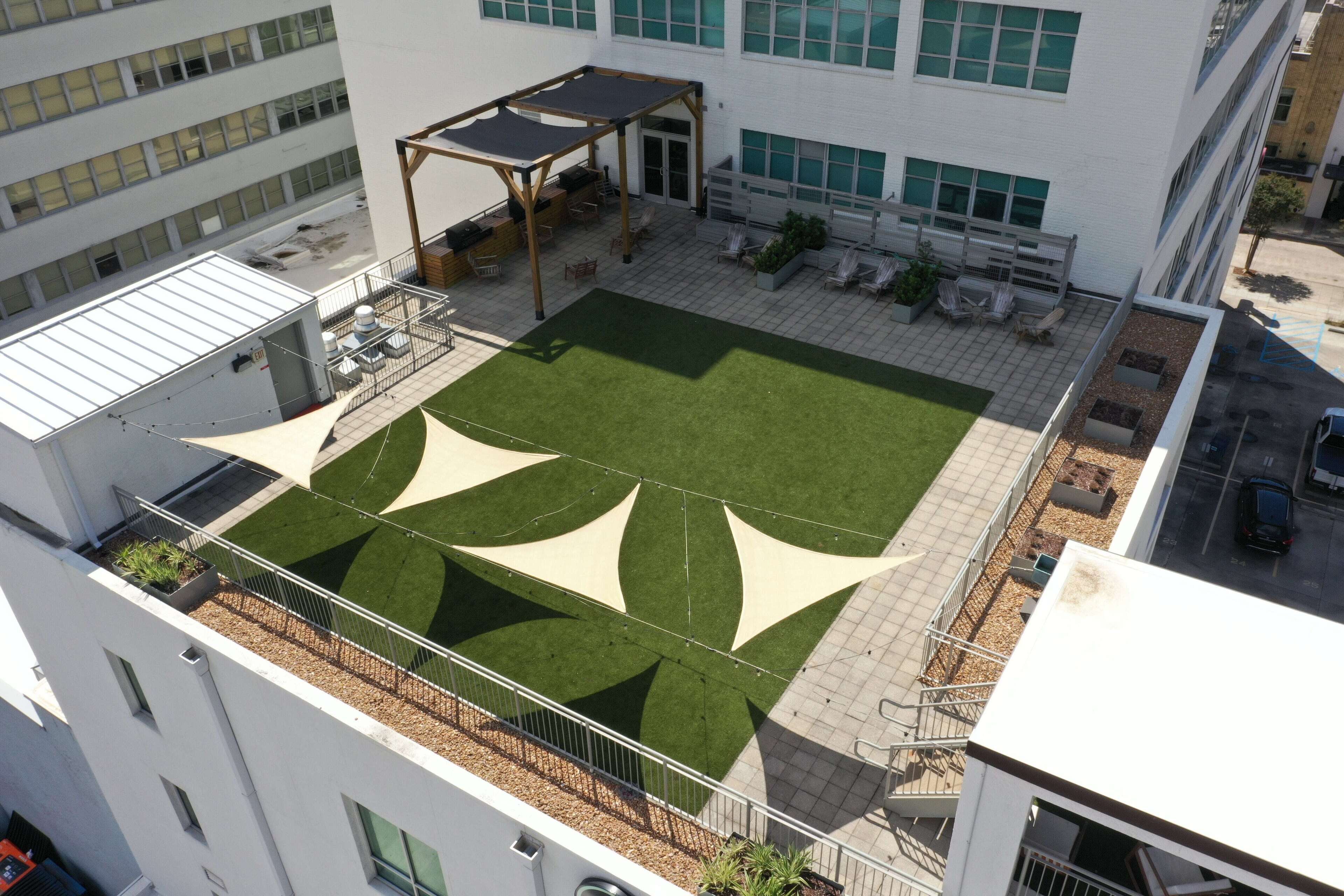 Vue aérienne d’une terrasse sur le toit, avec une pelouse verdoyante, un espace salon et une pergola.