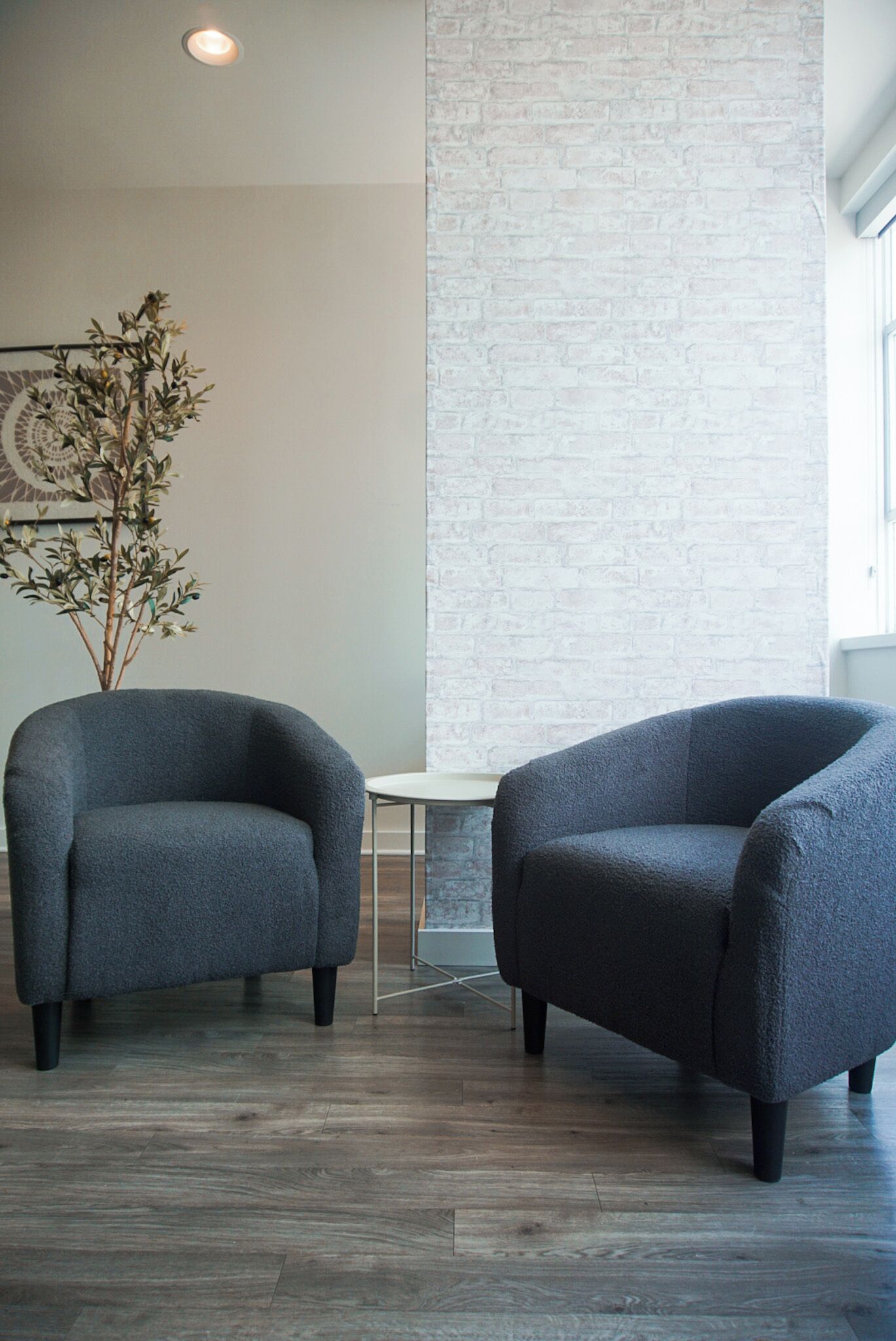Two dark grey armchairs, a small round table, and a tall white column in a modern room with wooden flooring.
