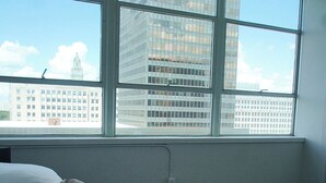 A hotel room with a large window, a bed with white linens, and a view of a cityscape. - StayAE - High Rise (Baton Rouge)