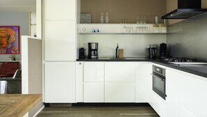 A modern kitchen with white cabinetry, a built-in oven, a coffee maker, and a range hood. - Bungalowpark It Wiid by Interhome (Eernewoude)