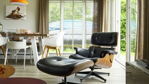 A modern living room with a black leather chair, a wooden dining table, white chairs, and a large window with blinds. - Bungalowpark It Wiid by Interhome (Eernewoude)