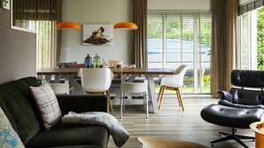 A modern living room with a sofa, a black leather chair, a dining table with chairs, and a large window with curtains. - Bungalowpark It Wiid by Interhome (Eernewoude)