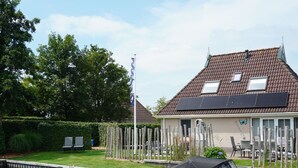A house with a tiled roof, solar panels, a flag, and a boat docked by a canal. - Bungalowpark It Wiid by Interhome (Eernewoude)