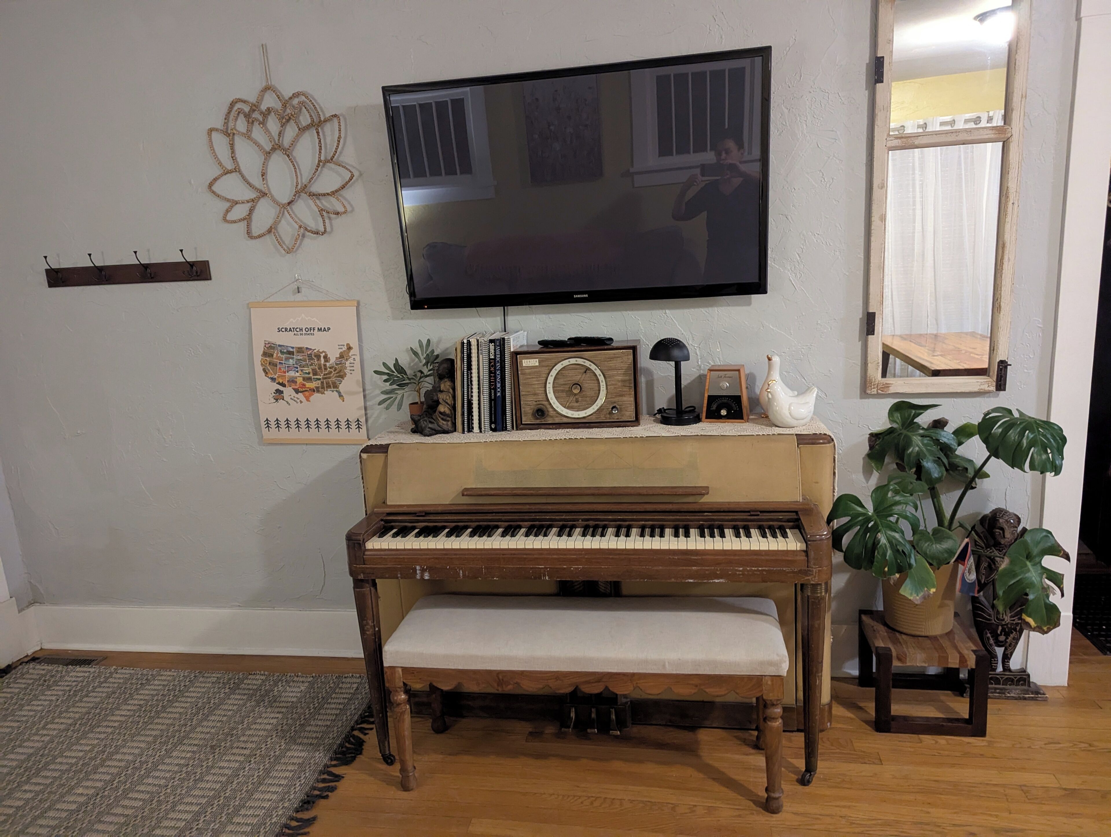 A room with a piano, a television, a decorative wall piece, a framed map, and a plant.