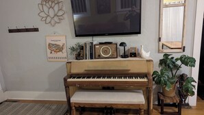 A room with a piano, a television, a decorative wall piece, a framed map, and a plant. - Remodeled Historical Home 2 blocks from CSU campus and 3 blocks to Old Town  (Fort Collins)