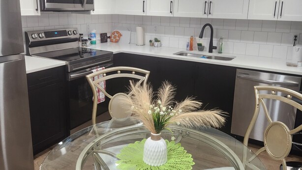 Una cocina moderna con armarios blancos, electrodomésticos de acero inoxidable y una mesa de comedor de vidrio con sillas.