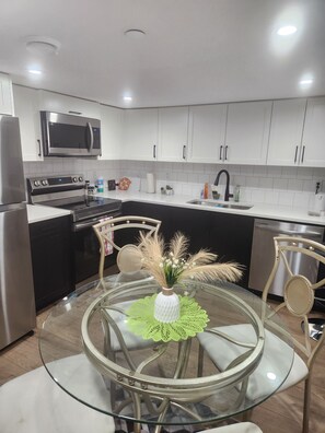 Una cocina moderna con armarios blancos, electrodomésticos de acero inoxidable y una mesa de comedor de vidrio con sillas.