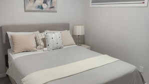 Un dormitorio con cama, mesita de noche, lámpara, ventana con persianas y un cuadro en la pared.