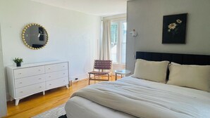 A bedroom with a bed, dresser, chair, and a painting on the wall.