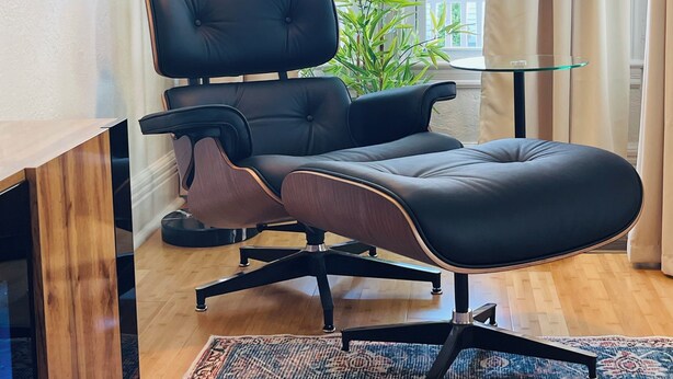 A modern living room with a black leather sofa, a glass coffee table, a patterned rug, and a floor lamp.