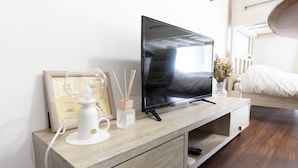 Un mueble de televisión de madera con un televisor de pantalla plana, un cuadro enmarcado, un candelabro blanco y un florero con flores secas.