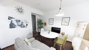 Una sala moderna con un sofá gris, una mesa de comedor redonda y un televisor.