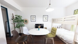Una habitación moderna con literas, una mesa redonda con sillas, una planta en maceta e impresiones botánicas enmarcadas en la pared.