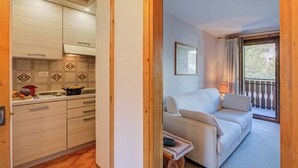 A kitchen with wooden cabinets, a dining table with fruits, and a sofa in a living area with a balcony view. - Casa Ciuk, Livigno, Italy (Livigno)