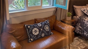 A cozy living room with a brown leather sofa, a window with blue curtains, and a small side table with a plant. - Santa Barbara Mission Studio (Santa Barbara)