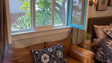 A cozy living room with a brown leather sofa, a window with blue curtains, and a small side table with a plant.
