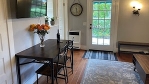 A dining area with a dark wooden table, chairs, a vase with flowers, a clock, and a door with a view of greenery. - Santa Barbara Mission Studio (Santa Barbara)