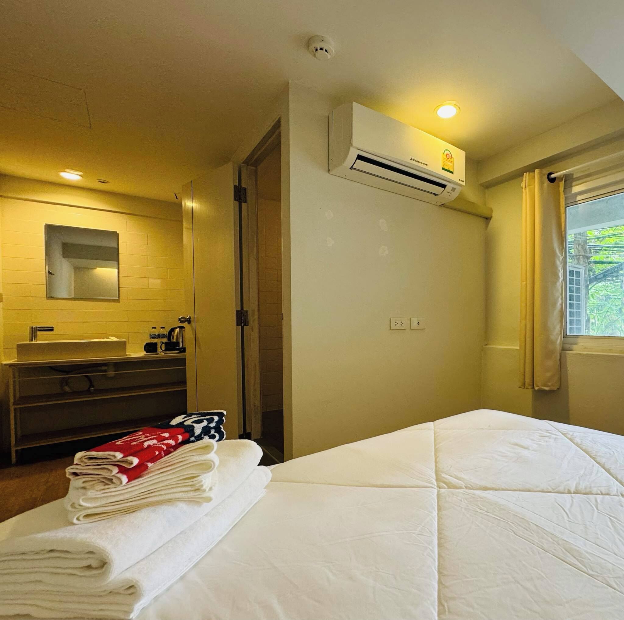 A hotel room with a bed, a bathroom with a sink and mirror, and an air conditioning unit.
