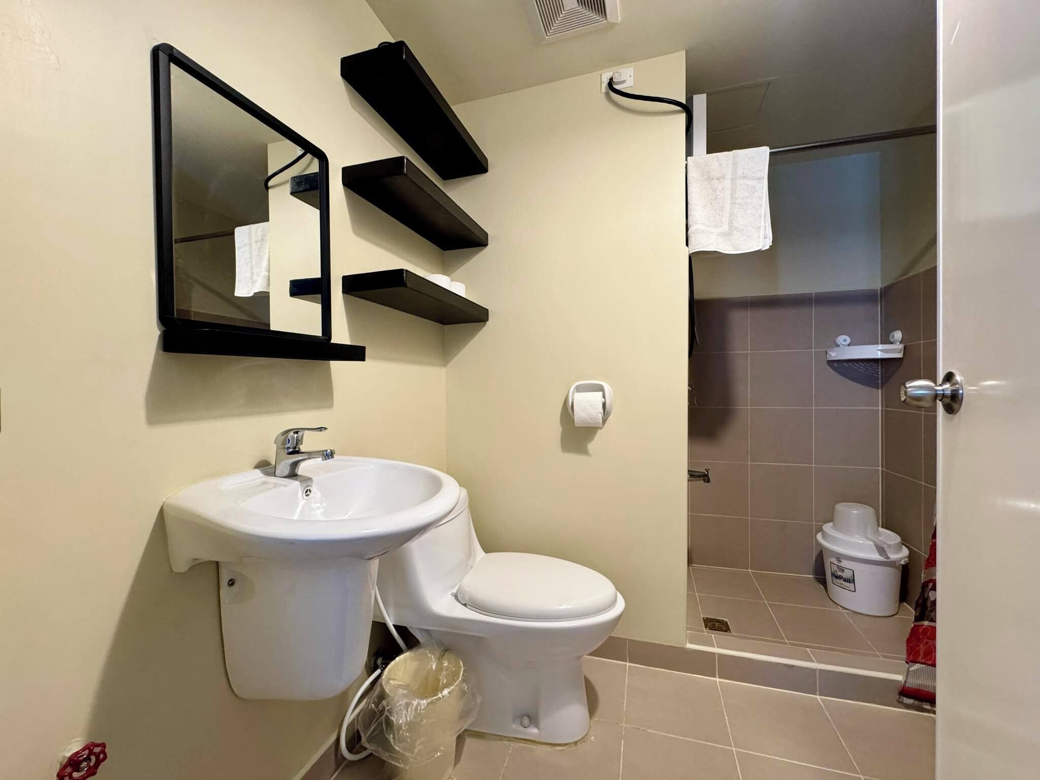 A bathroom with a sink, toilet, and a shower area. There are shelves above the sink and a towel hanging on the shower door.