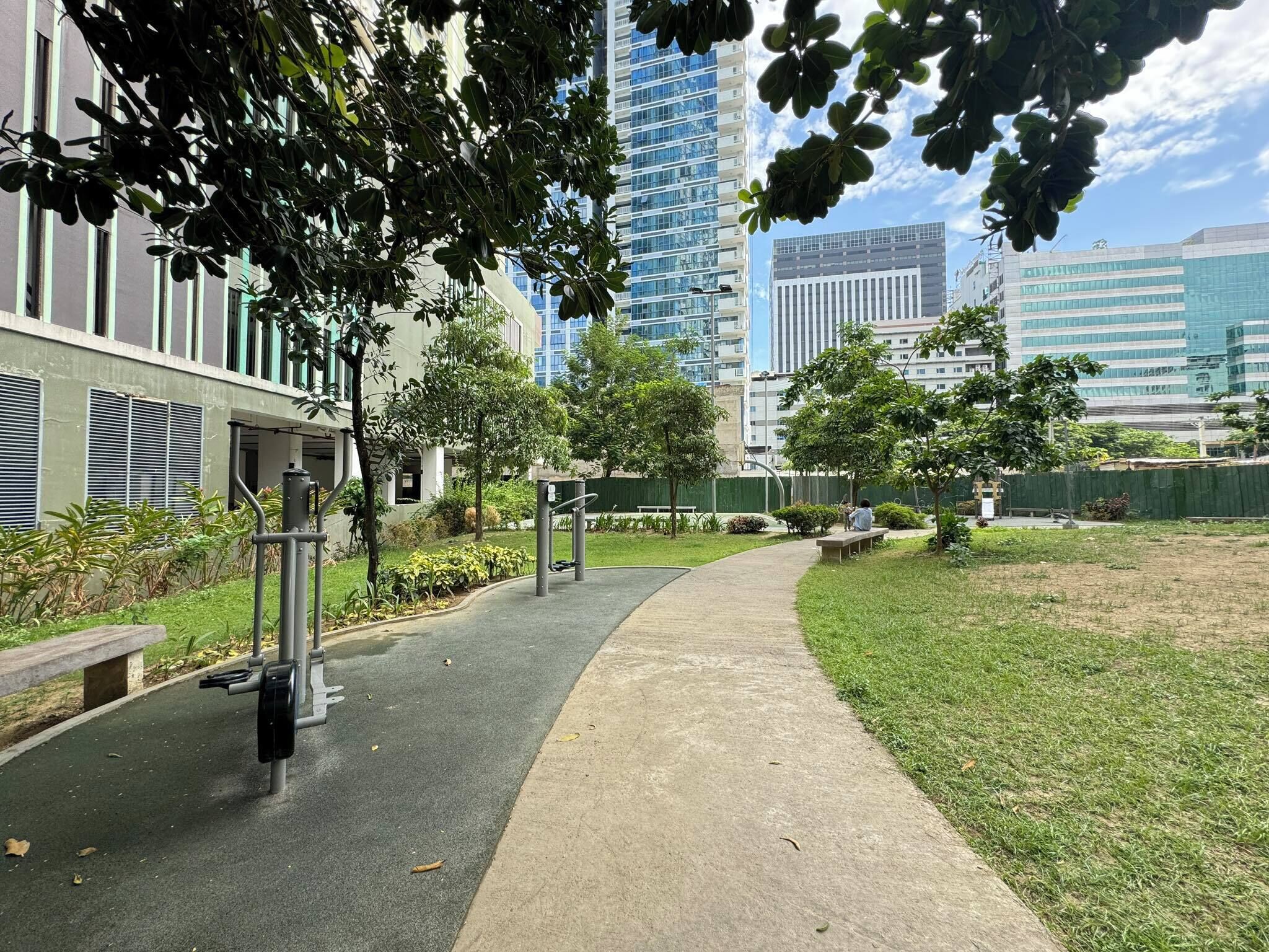A pathway leading to a building with a modern design, surrounded by greenery and a fenced area.