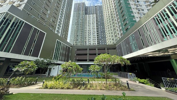 A modern high-rise building with multiple floors, large windows, and a central courtyard with greenery. - Condotel Avida Riala Tower 4-1103 (Cebu City)