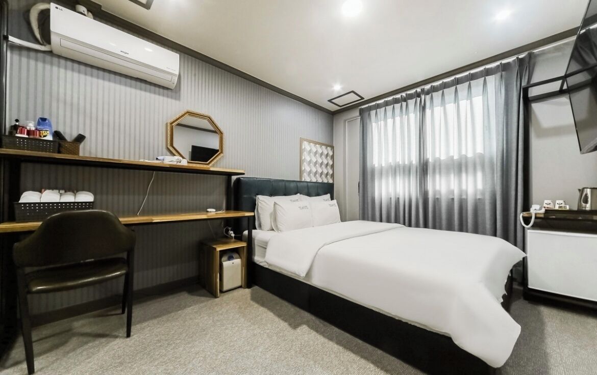 A hotel room with a bed, a desk, a chair, a TV, and a window with curtains.