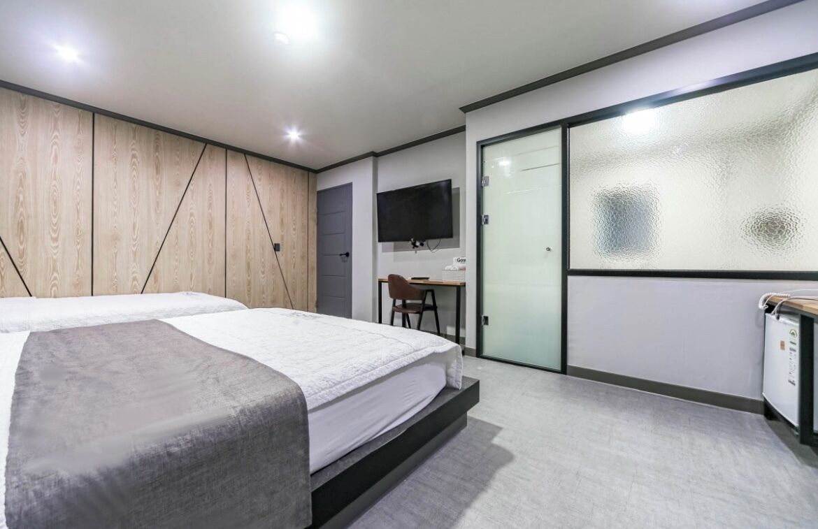 A modern hotel room with a bed, a desk, a chair, and a television.