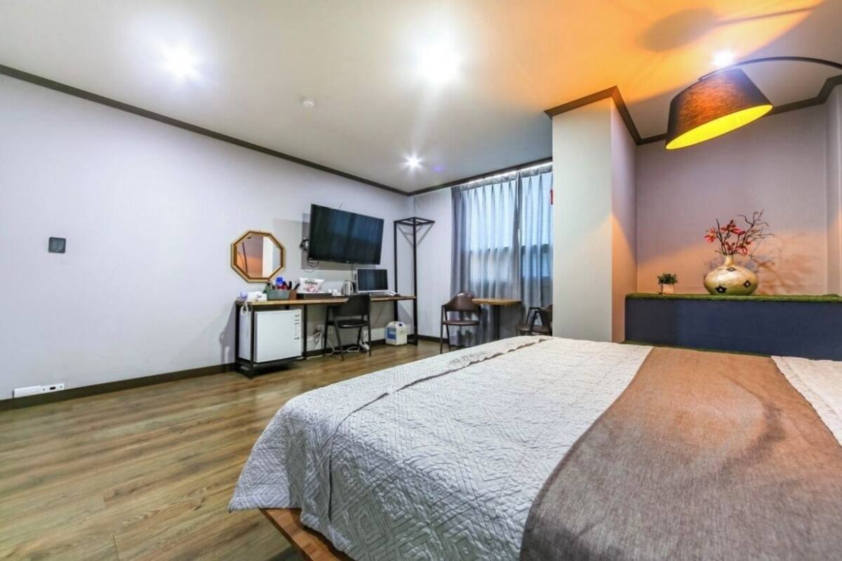 A hotel room with a bed, desk, chair, TV, and a lamp.