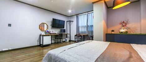 A hotel room with a bed, desk, chair, TV, and a lamp.