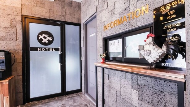 A hotel entrance with a glass door, a sign with the hotel's name, and a counter with a rooster decoration. - The Sharp Hotel (Changwon)