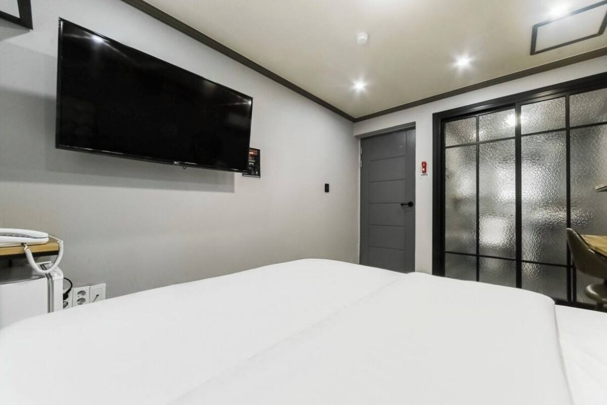 A hotel room with a bed, a TV mounted on the wall, a desk with a chair, and a door with frosted glass panels.