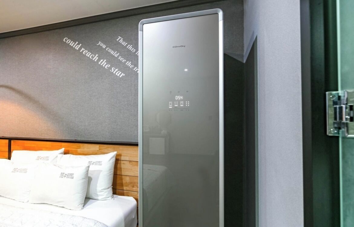Una habitación de hotel moderna con un espejo grande, una cama con ropa de cama blanca y una frase motivacional en la pared.