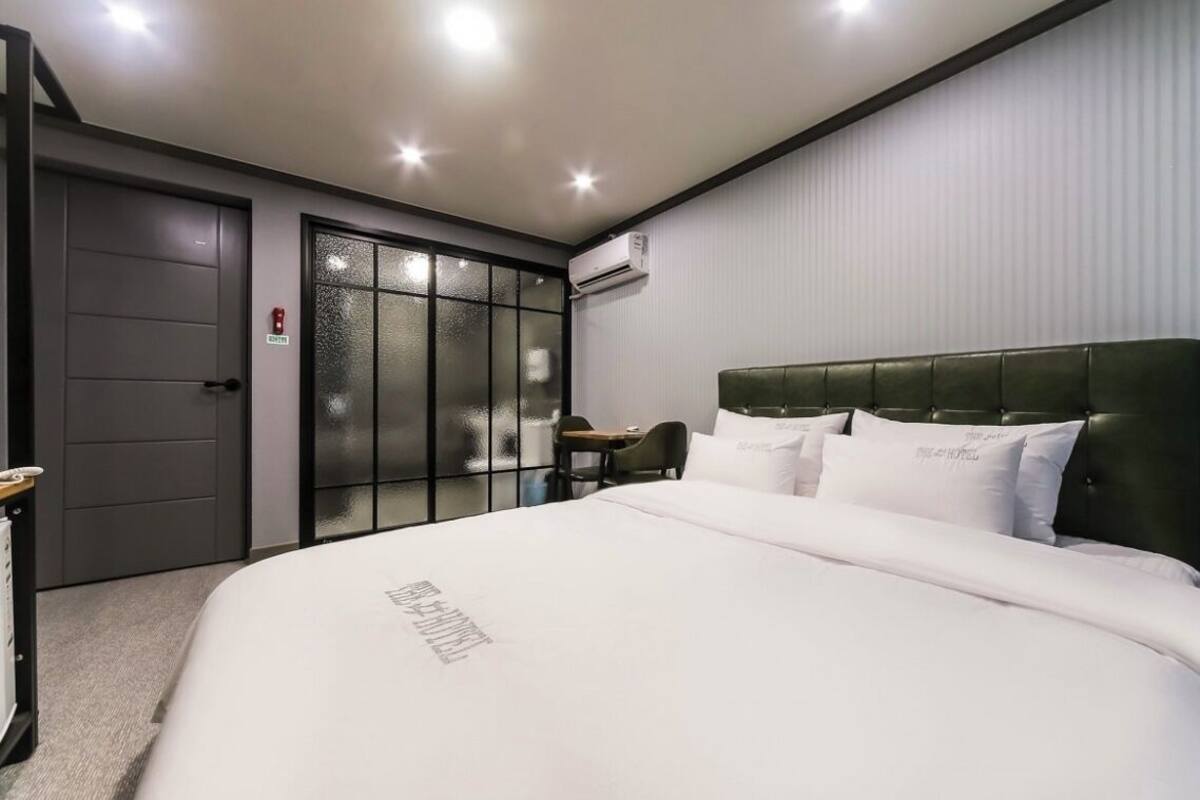 A hotel room with a large bed, a small desk, a chair, a wardrobe, and an air conditioning unit.