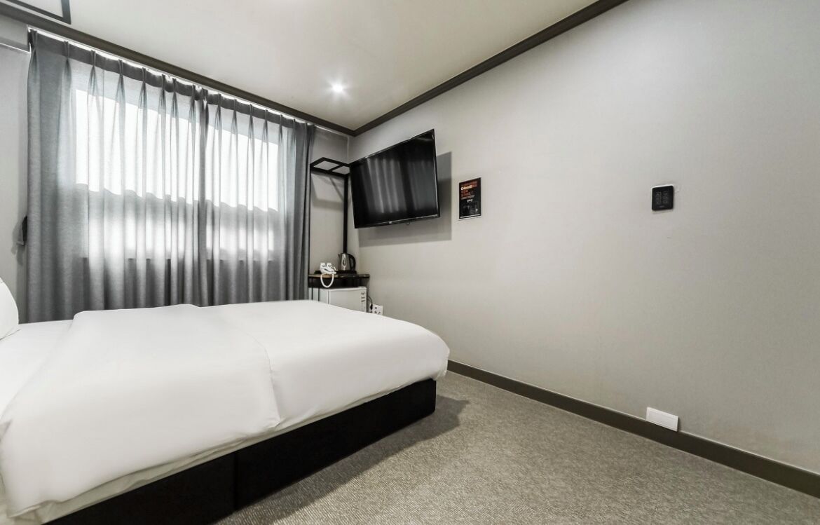 Une chambre d’hôtel avec un lit, un téléviseur fixé au mur, une petite table et une fenêtre avec des rideaux.
