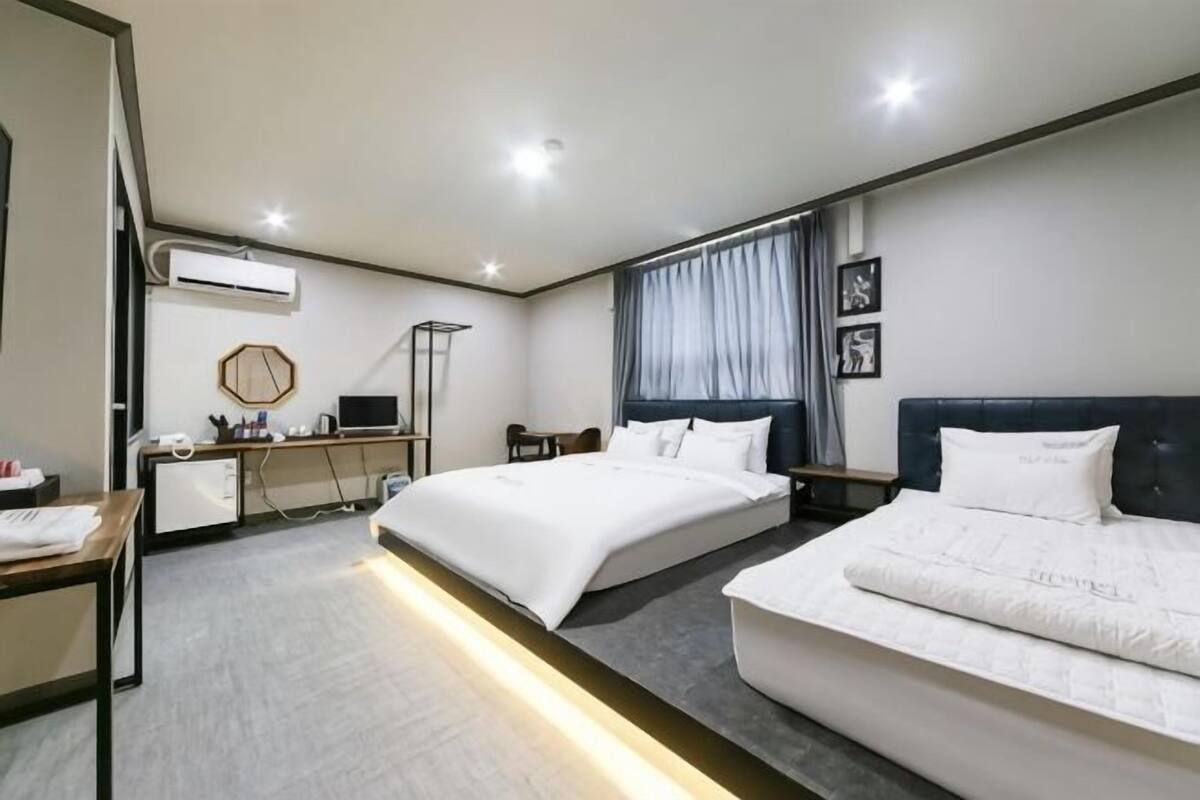 A hotel room with two beds, a desk, a chair, a lamp, and a window with curtains.