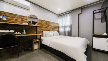 A hotel room with a bed, a desk with a chair, a mirror, a TV, and a window with curtains.