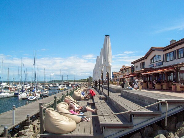 A wooden pier with seating areas and umbrellas, overlooking a marina with boats.
